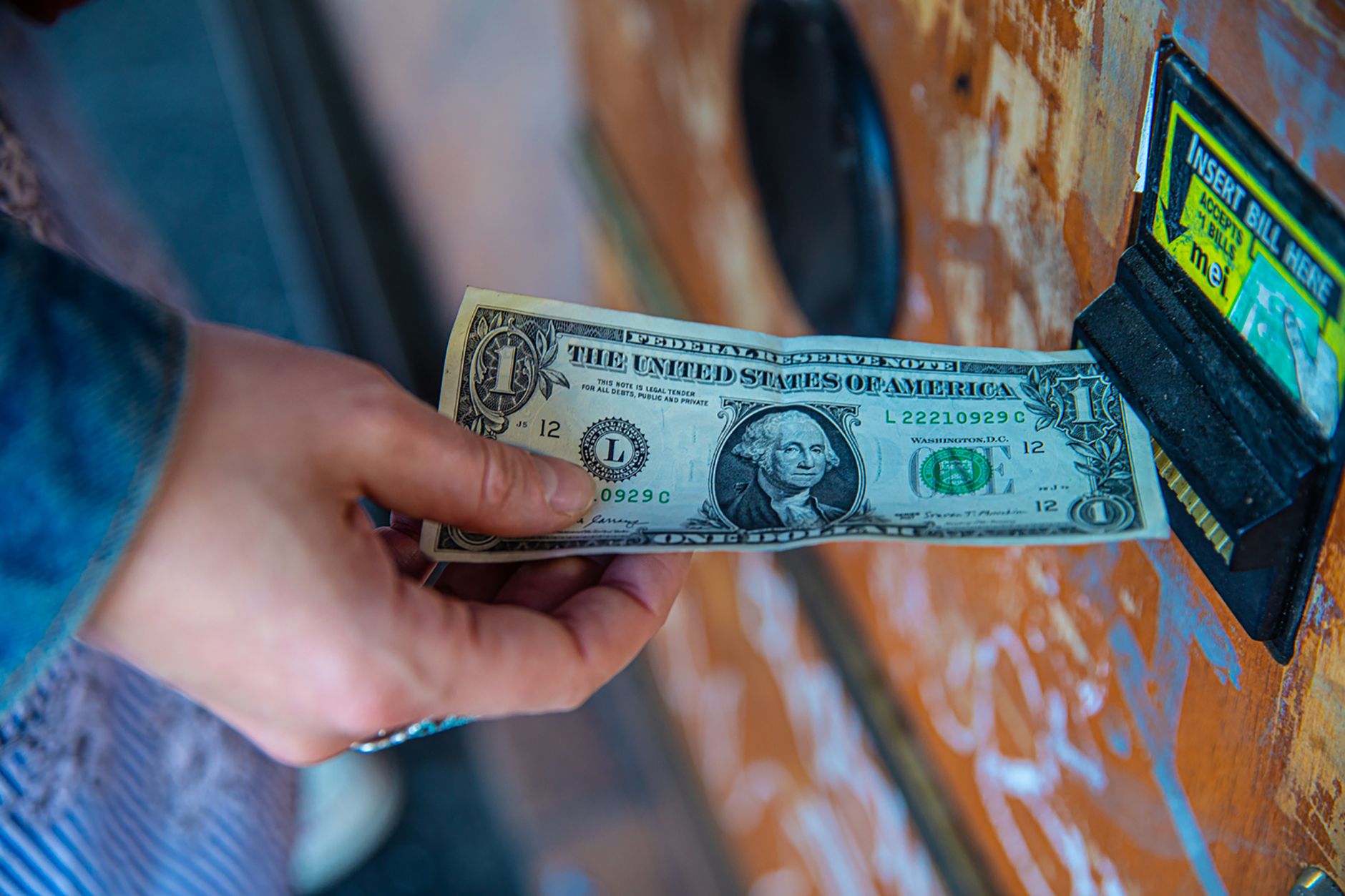 A person inserting a US dollar bill into a vending machine slot, capturing a financial transaction moment.