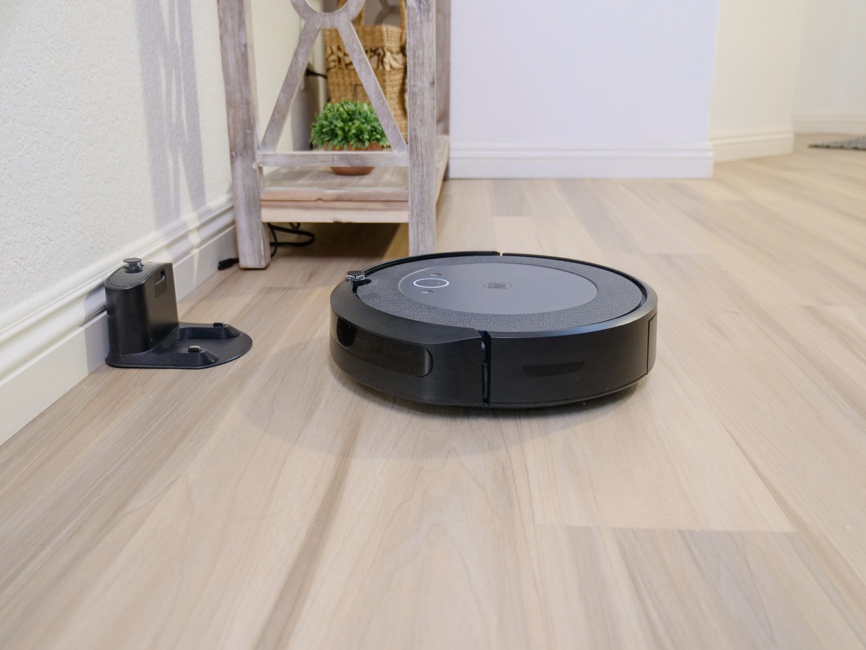 A sleek robotic vacuum navigates a clean hardwood floor beside a docking station.