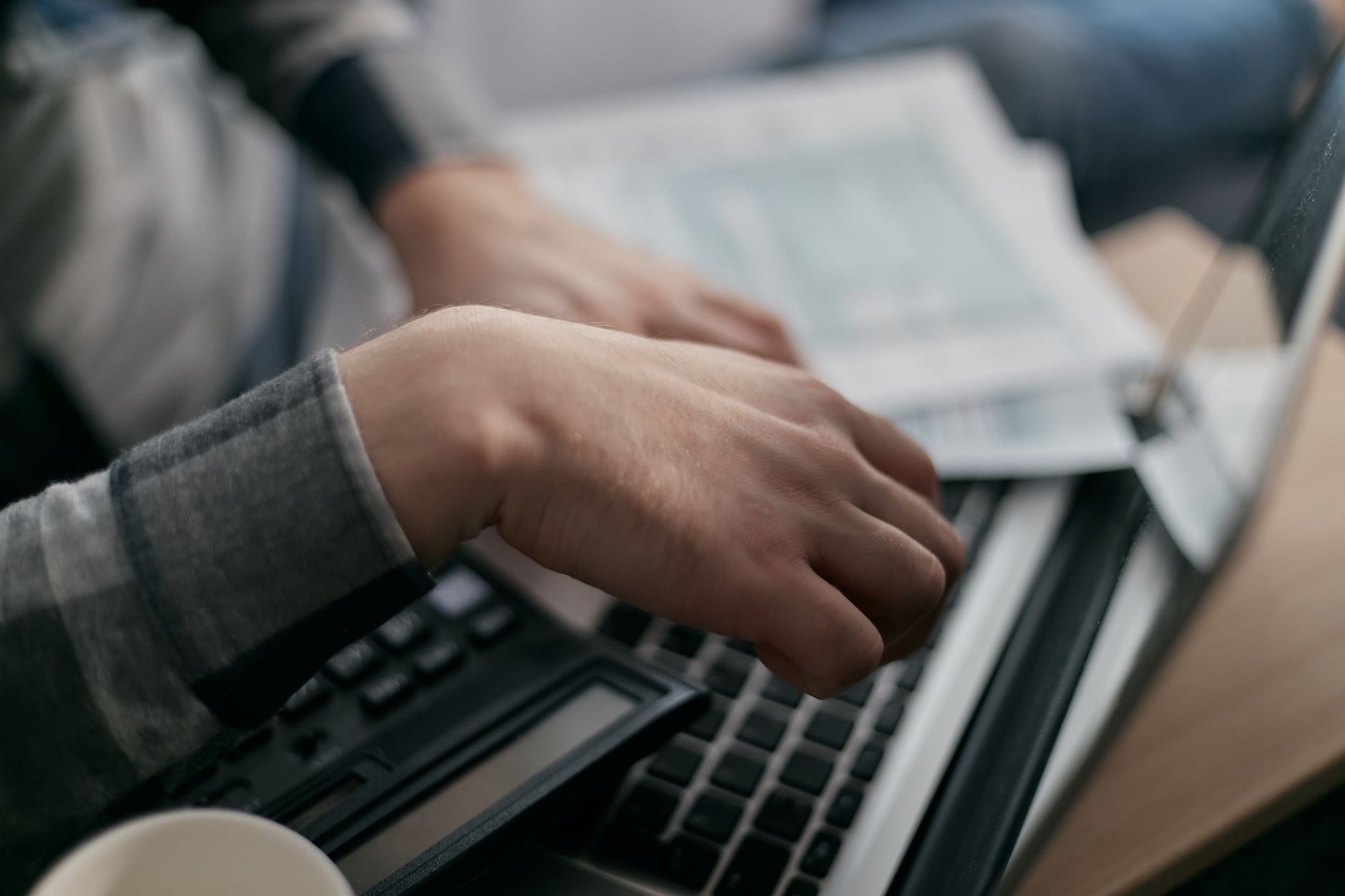 Close-up of hands calculating finances with a laptop and paperwork.