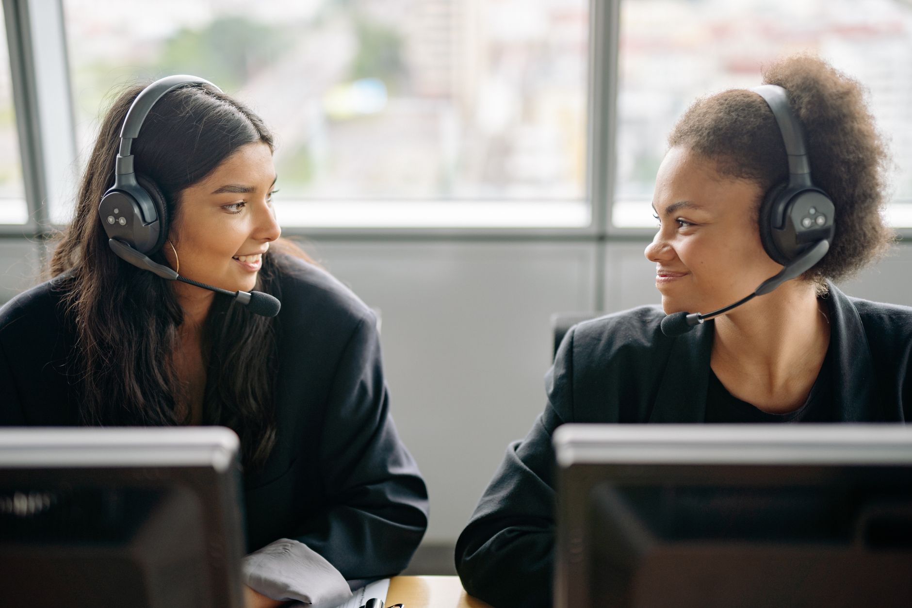 Two smiling female call center agents with headsets engaging in teamwork.
