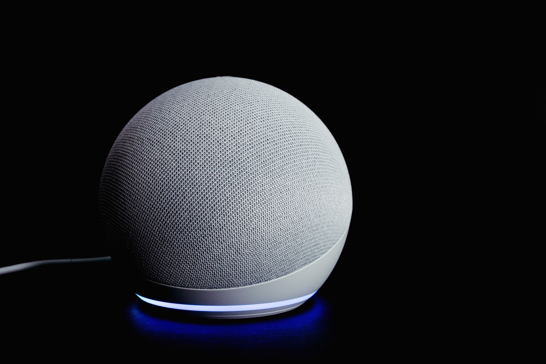 Modern smart speaker device with illuminated ring, featured on a dark background.