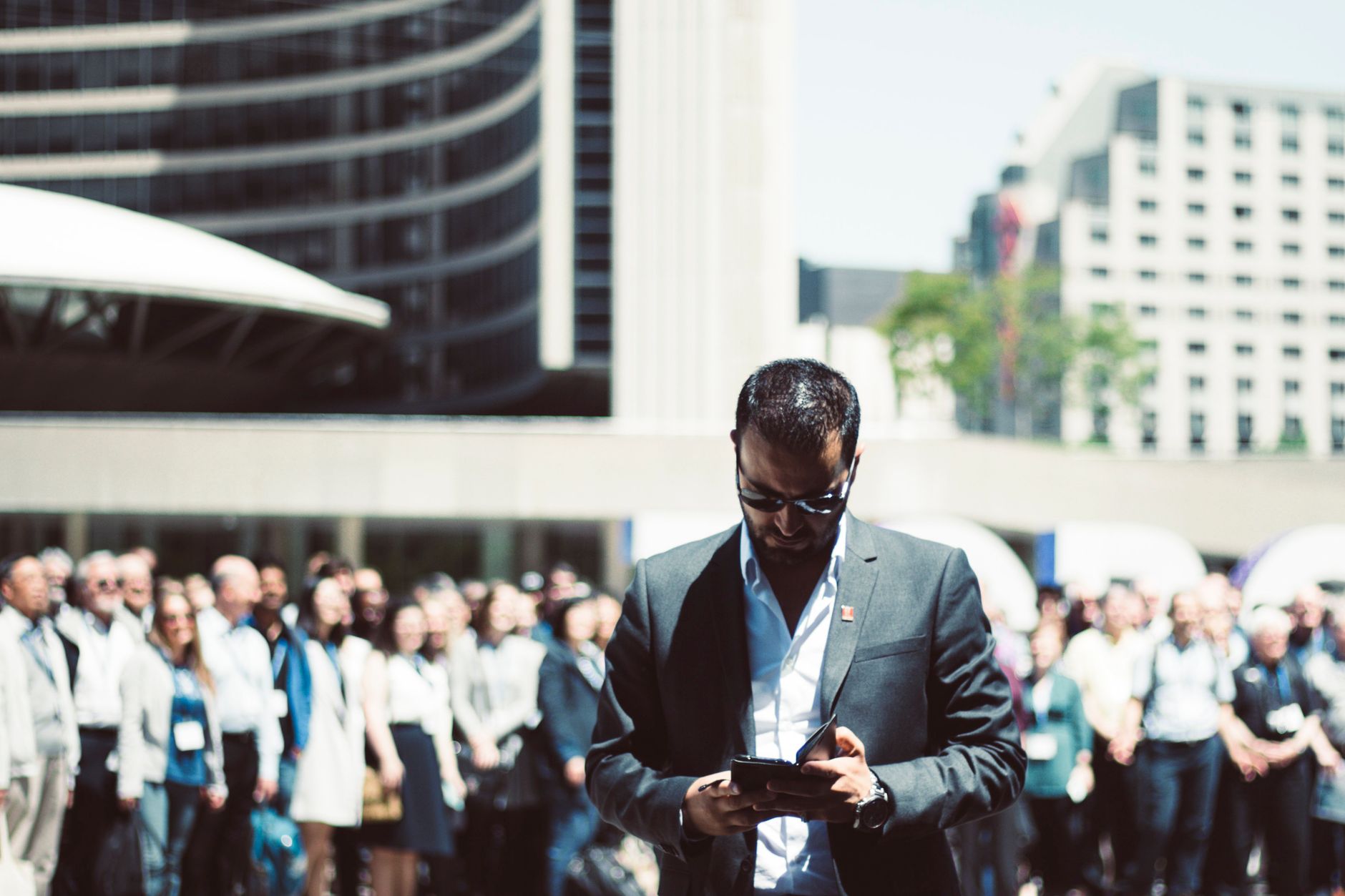 Focused businessman using tablet in a bustling crowd in Toronto's busy urban setting.
