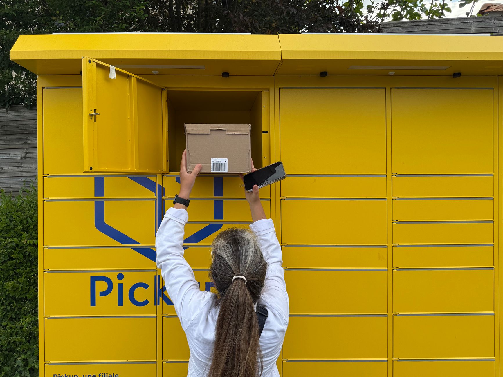 A woman using a yellow parcel locker to pick up a package in Périgueux, France.