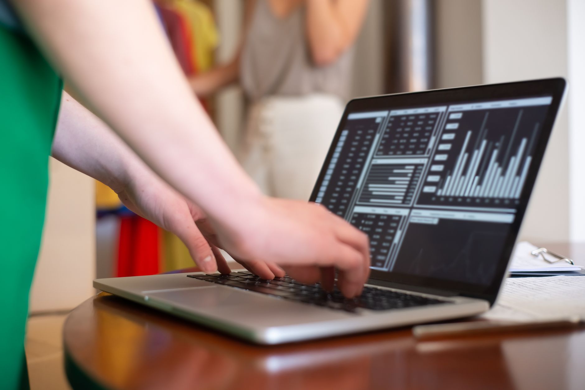 Hands typing on a laptop displaying data charts in an indoor setting.